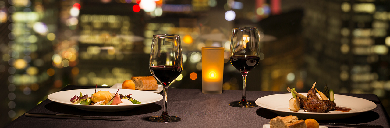 2 french cuisine dishes and 2 glass of red wine in the restaurant table by the window over looking city view